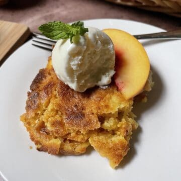Peach cobbler on a white plate with ice cream.