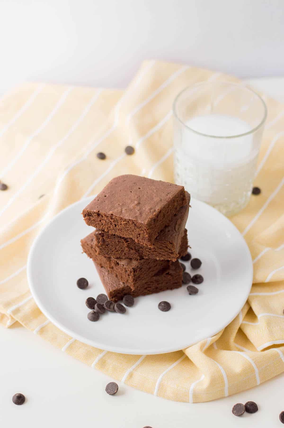Dark chocolate brownies on white table with yellow napkin and glass of milk.