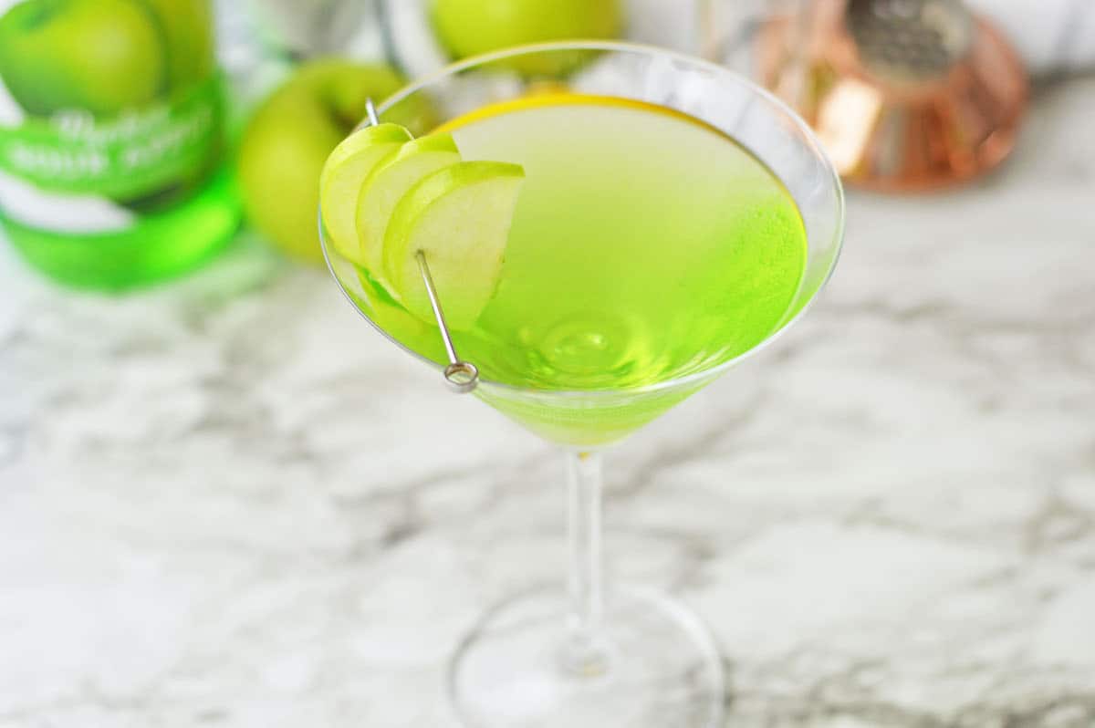 Green apple martini in martini glass with green apple slices.