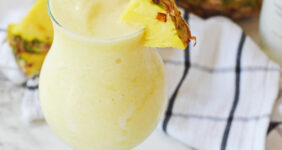 Pina colada with pineapple slice and 2 straws on marble table.