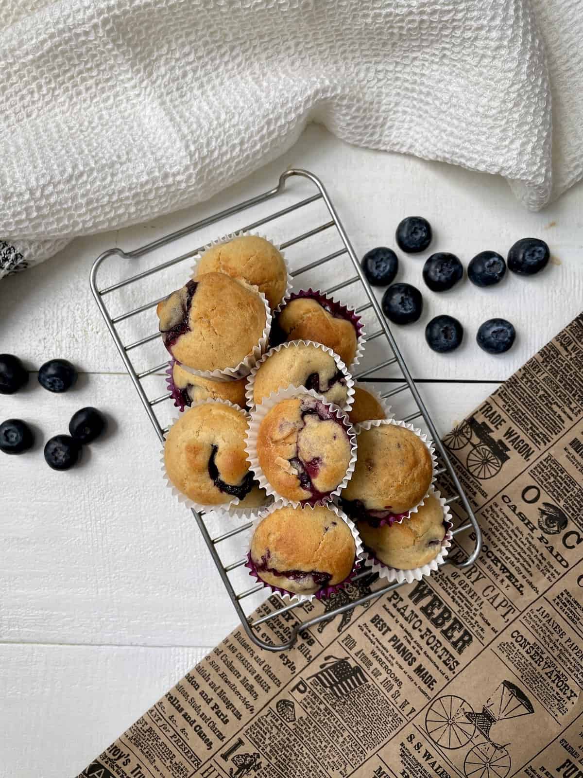 Blueberry muffins on a grate on a white table with newspaper and napkin.