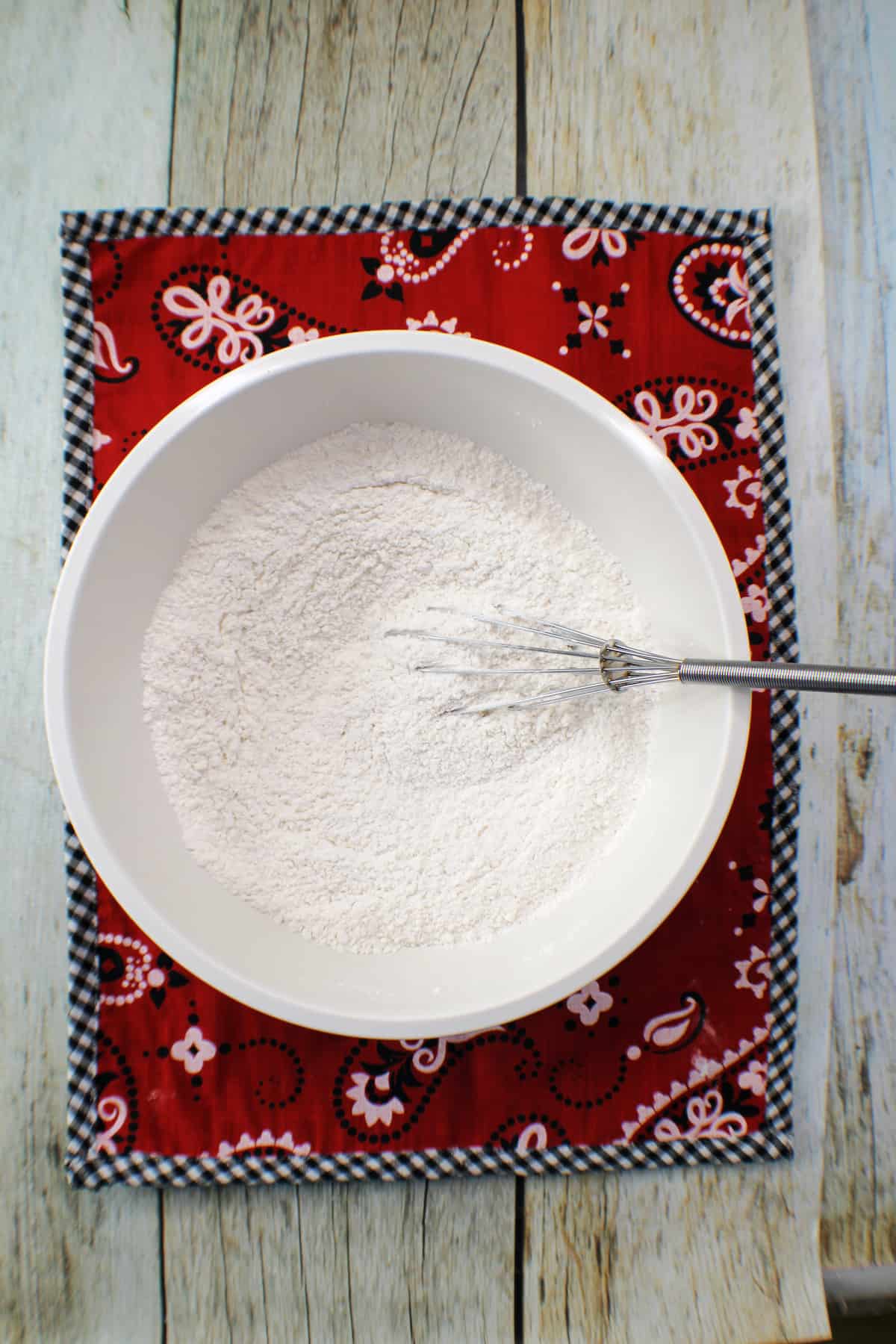 Dry cake ingredients in a bowl on a red kerchief on a wood table.
