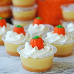Fall jello shots in plastic cups topped with pumpkins.