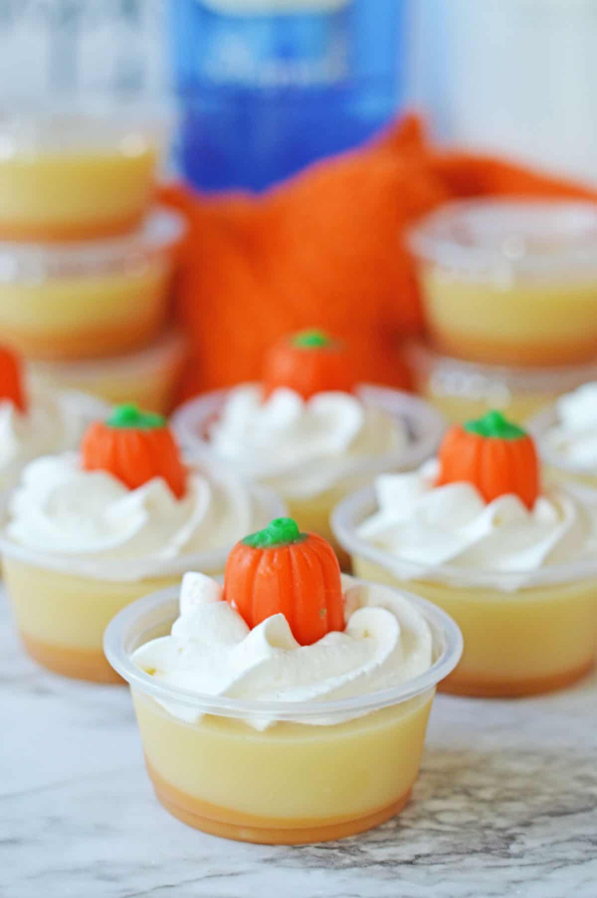 Pumpkin jello shots with whipped cream topped with pumpkin candy.