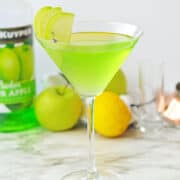 Green apple martini on white marble table.