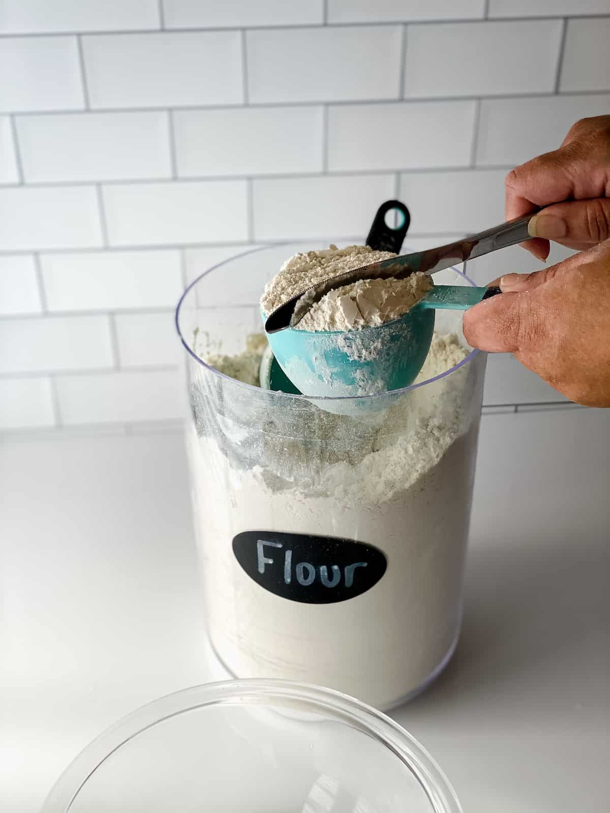 Container of flour and blue measuring cup being leveled.
