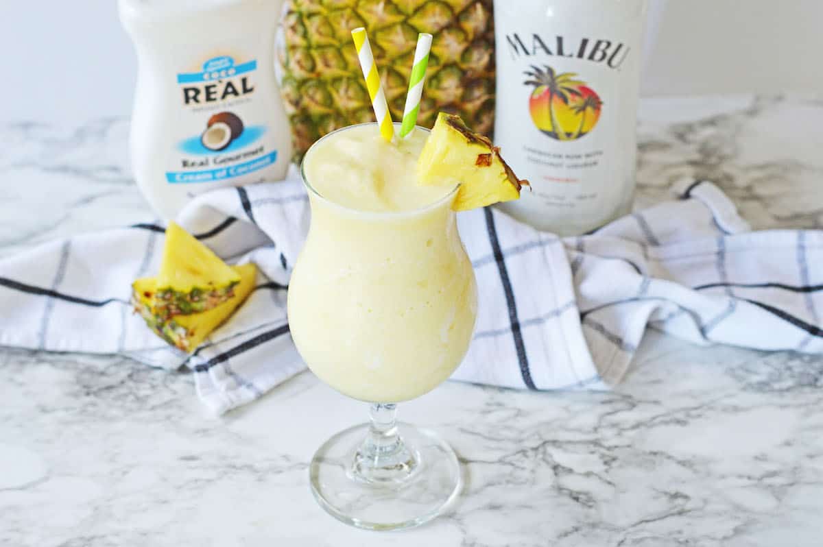 Pina colada with a slice of pineapple and two straws.