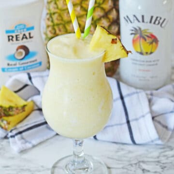 Frozen yellow cocktail with straws and pineapple slice.