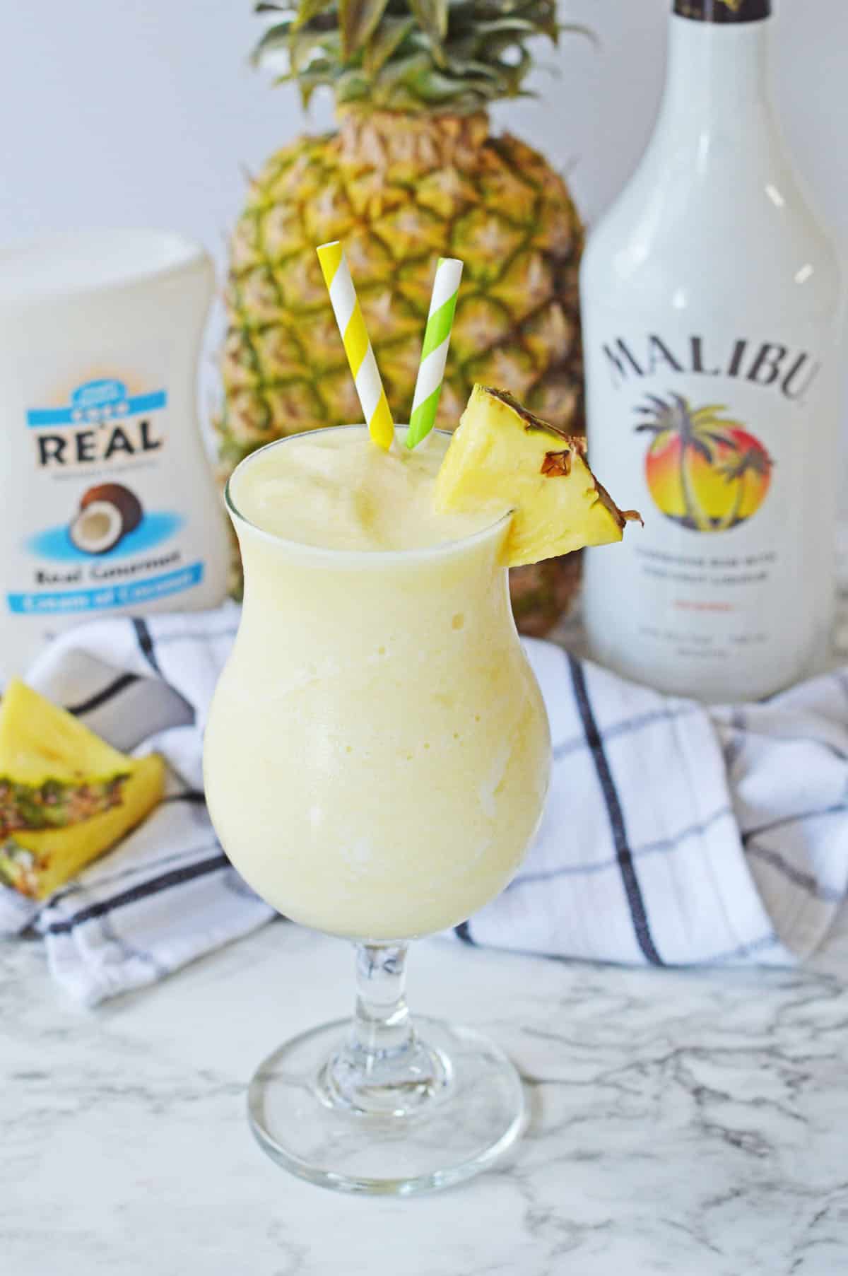 Frozen Pina Colada in a tall glass with pineapple and straws.
