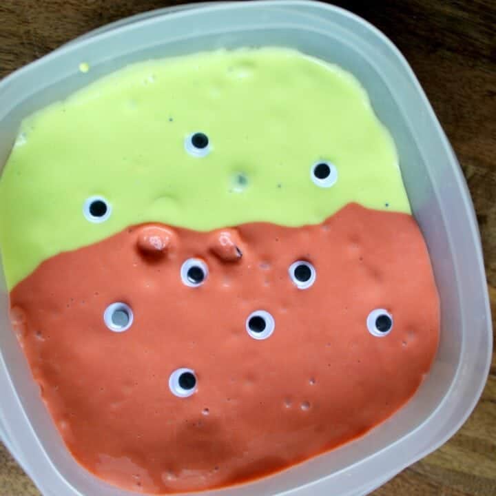 Plastic container of green and orange slime with googly eyes.