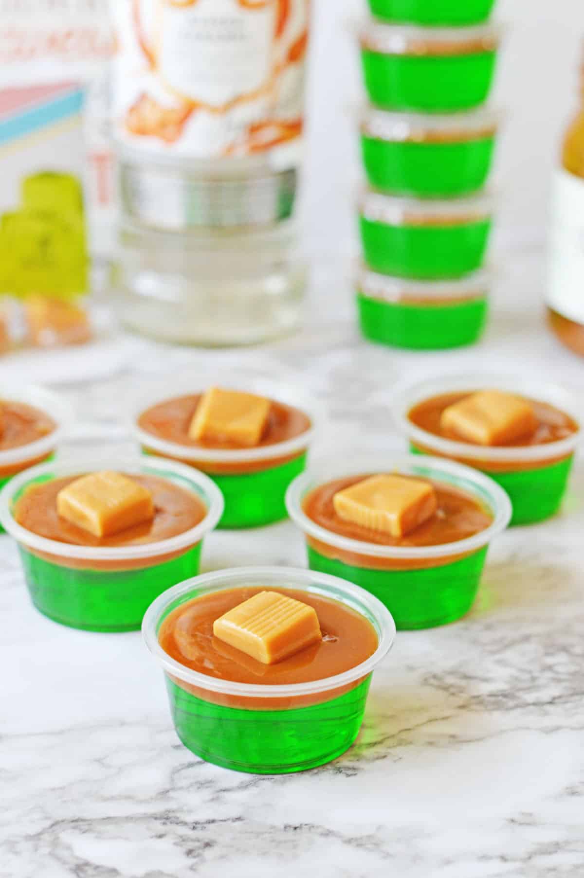 Green jello shots with a layer of caramel and caramel candy on top.