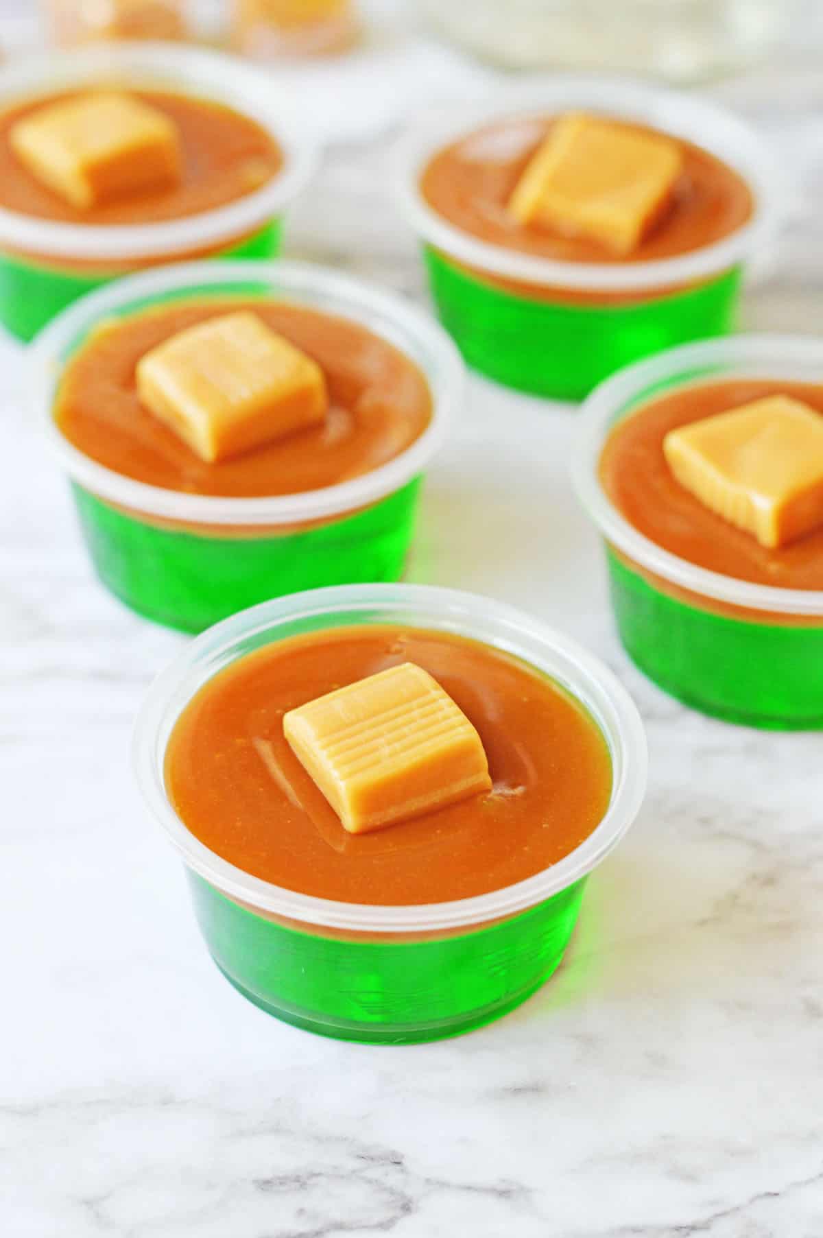 Green Jello shots with caramel layer and caramel candy on top.