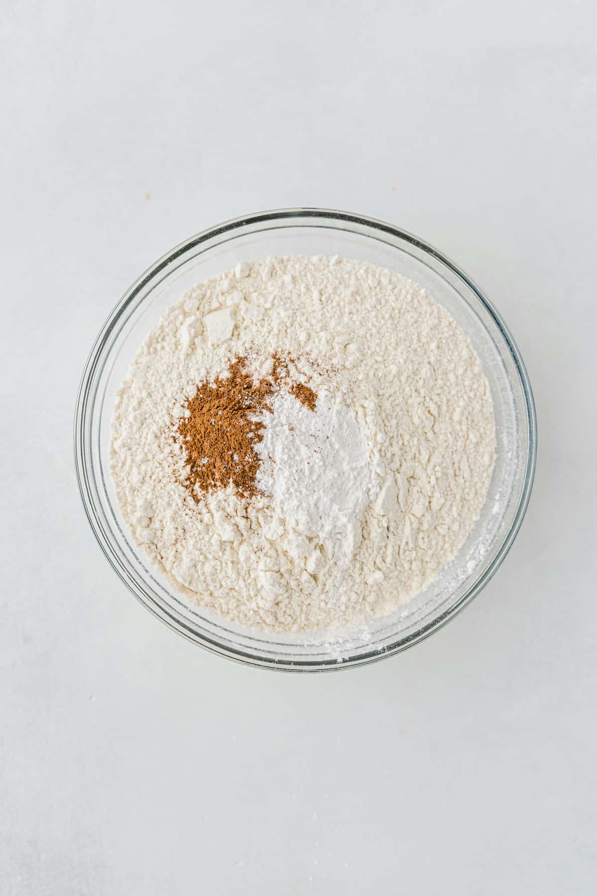 Flour, baking powder, cinnamon, and salt in a glass bowl.