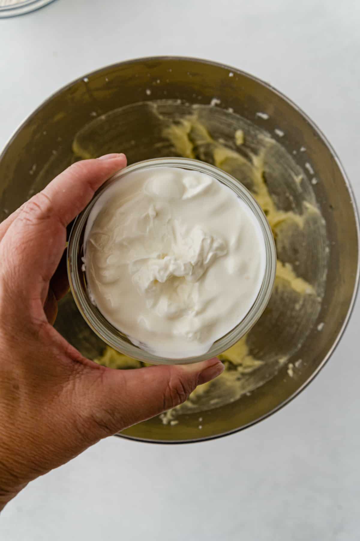Sour cream in bowl over larger bowl of muffin mixture.
