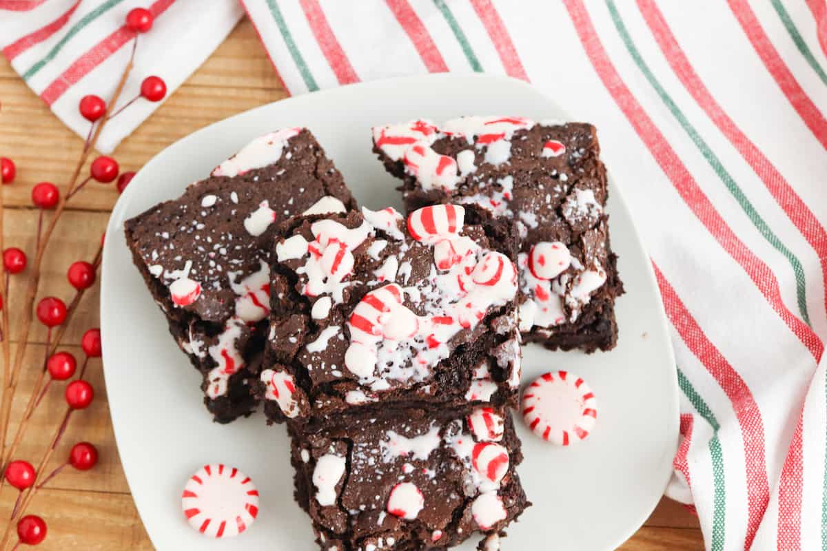 Brownies with candies on a white plate on wood table with striped dish towel.
