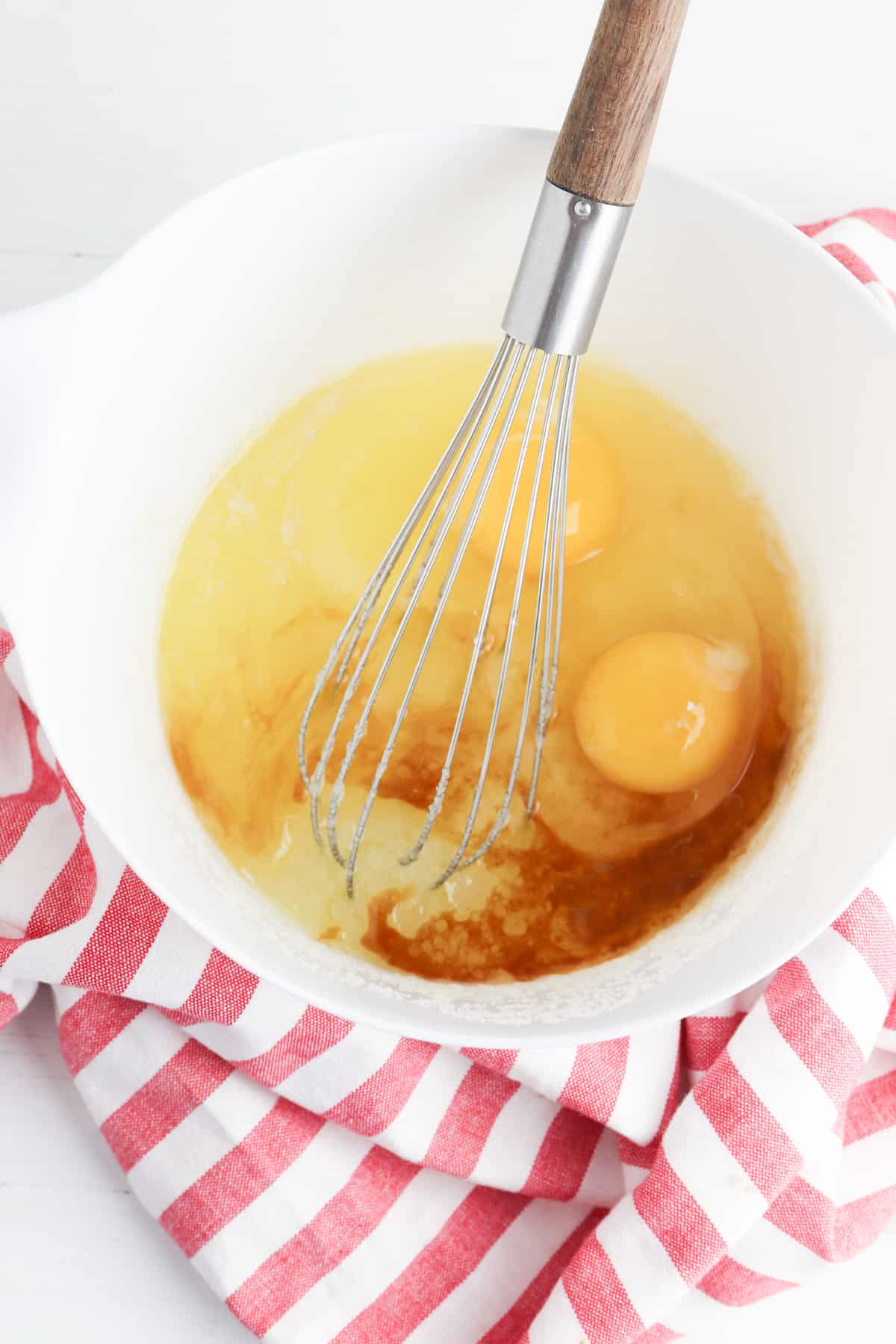 Sugar, butter, eggs in a white bowl on red striped cloth.