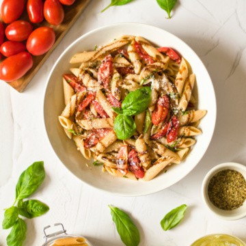 Margherita pasta with tomatoes and basil in a white bowl.
