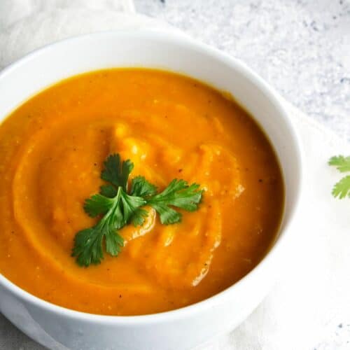 Sweet potato soup in a white bowl with parsley garnish.