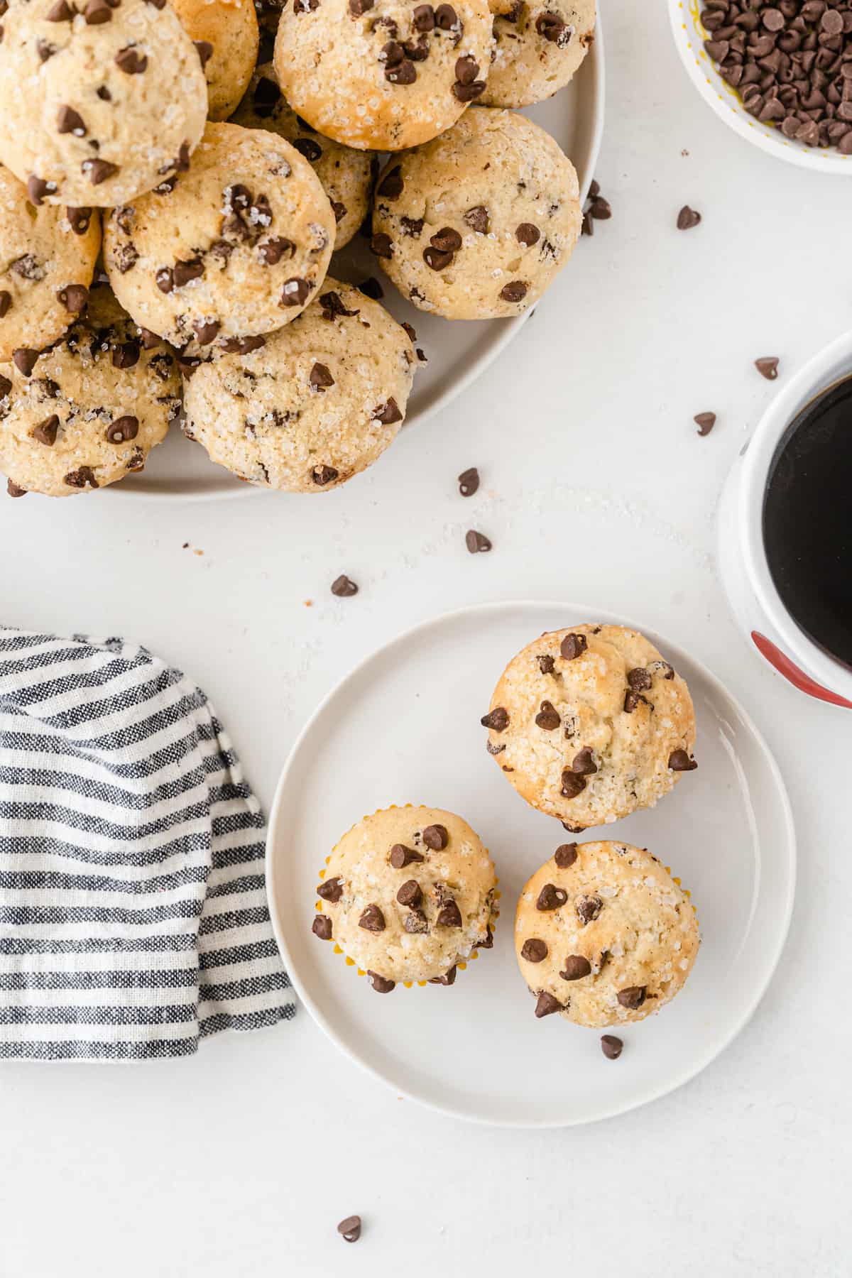 Mini chocolate chip muffins piled on a white plate on a white table. with coffee and muffins on a plate.