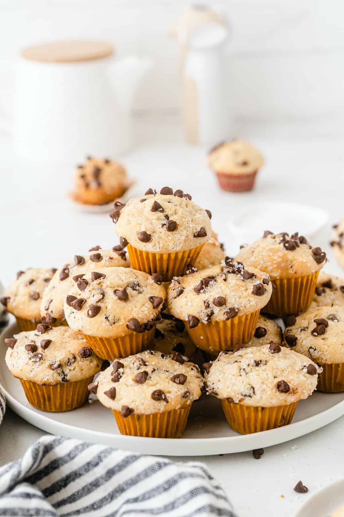 Mini chocolate chip muffins piled on a white plate on a white table.