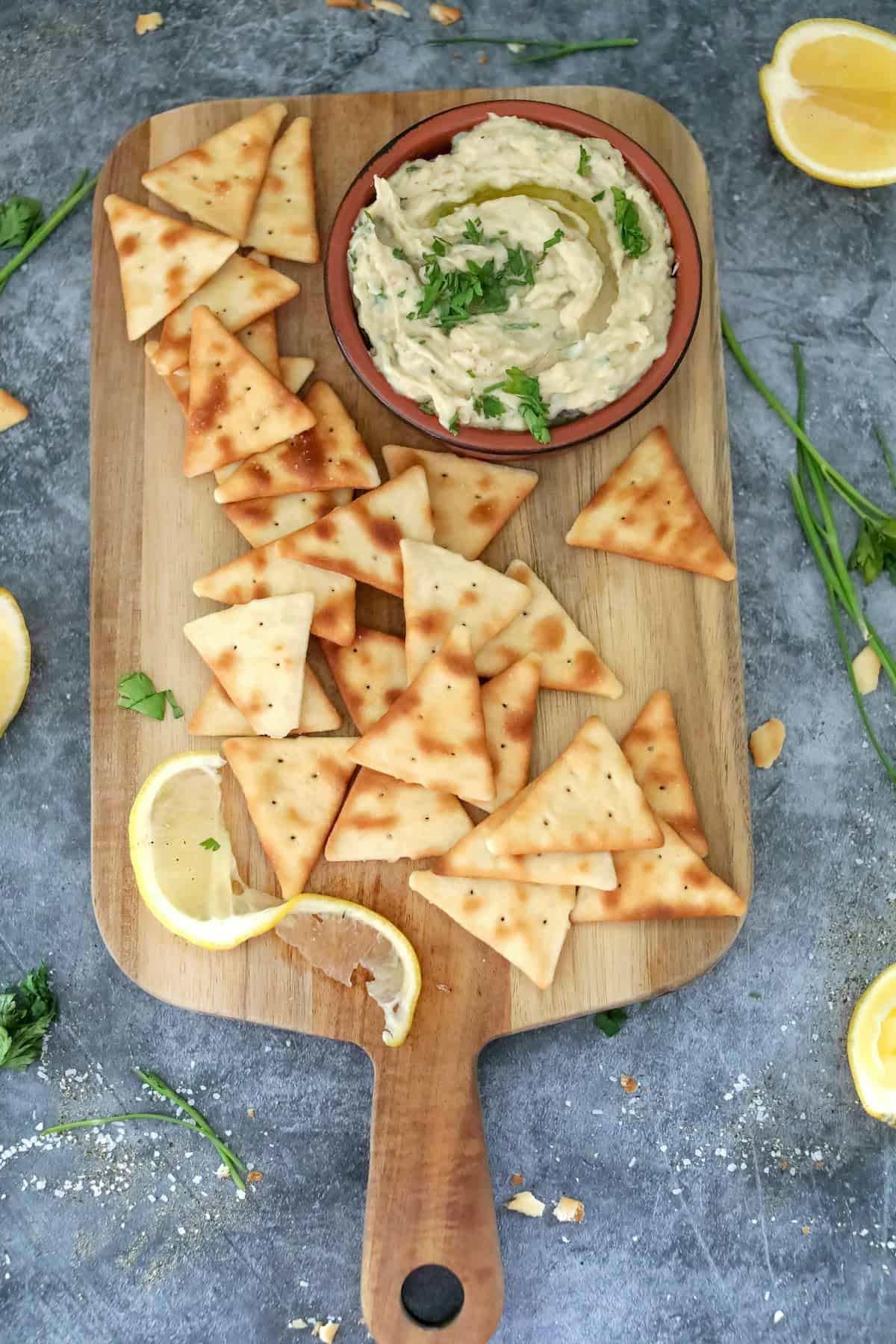 White dip with parsley in clay pot on wood cutting board with lemon.