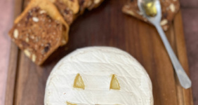 Brie cheese carved like a Jack O'Lantern on a wood board with crackers and honey for Pinterest.