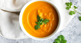 Sweet potato soup in a white bowl with parsley garnish for Pinterest.