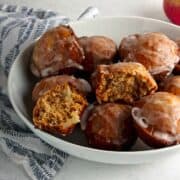 Apple fritters in a white bowl with a striped dish towel.
