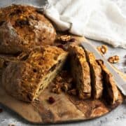 Loaf of bread on cutting board with white dish towel on side.