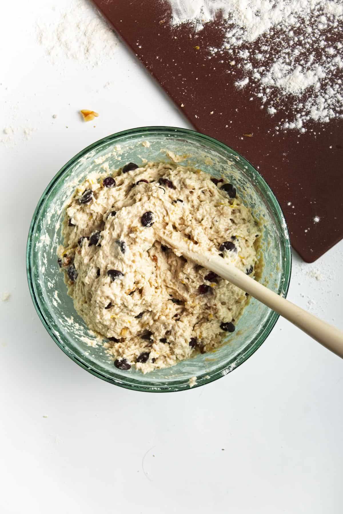 Wet dough with chocolate chips and cranberries in glass bowl.