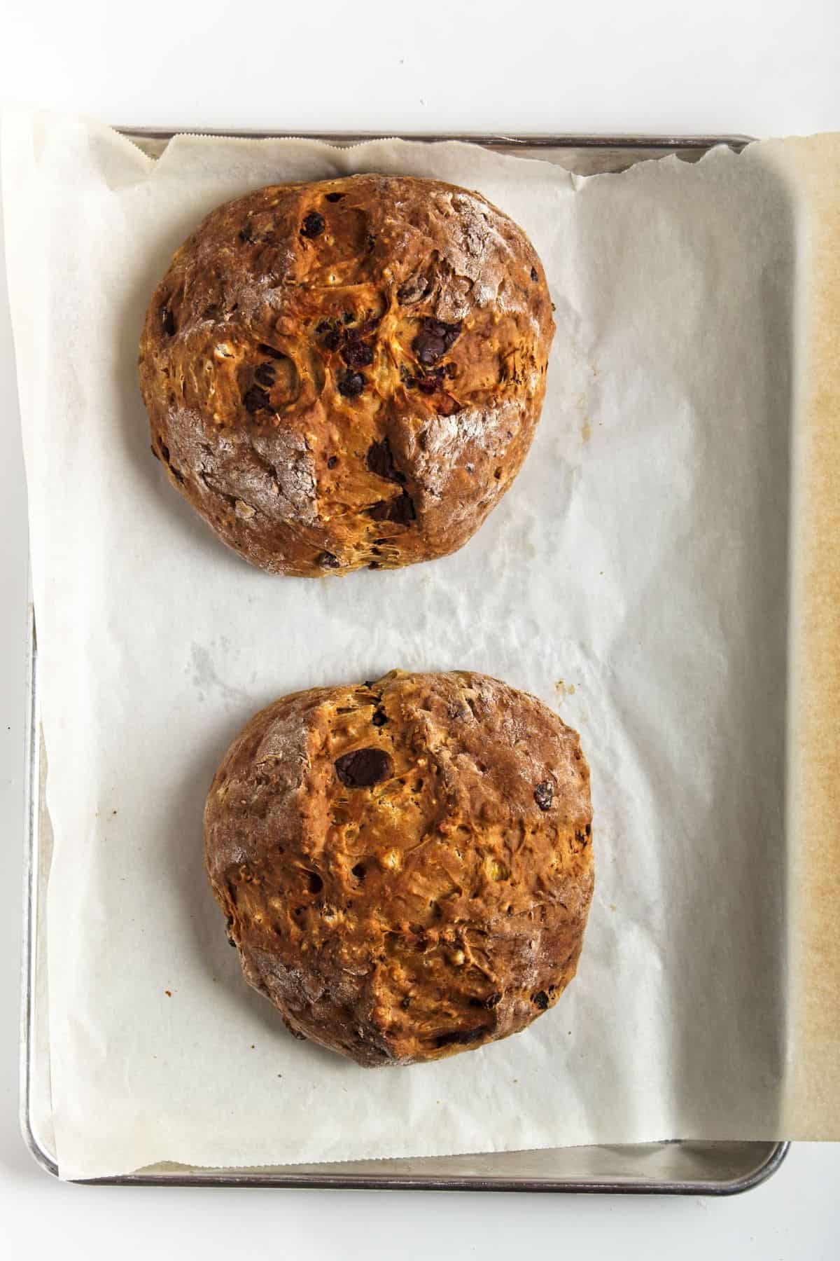 Two loaves of baked bread on parchment paper on baking sheet.