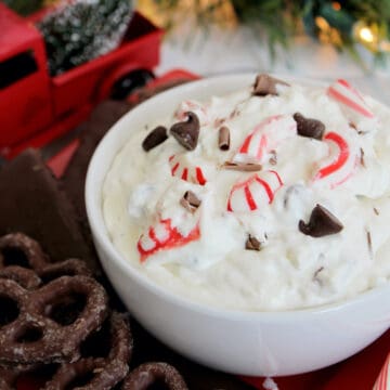 Bowl of dessert dip with peppermint, cream cheese, cool whip, mint, and chocolate on red tray.