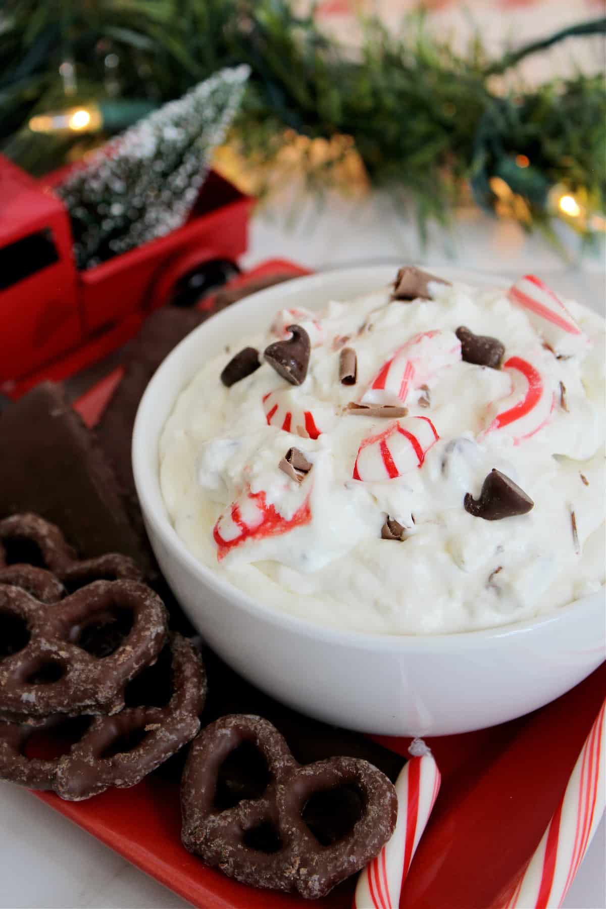 Bowl of dessert dip with peppermint, cream cheese, cool whip, mint, and chocolate on red tray.