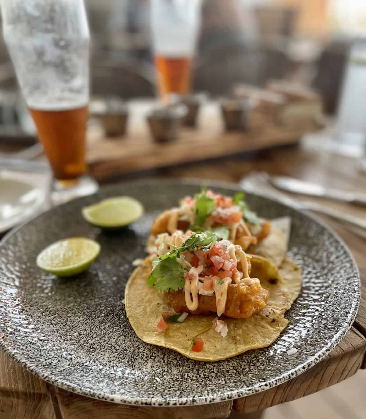 Tacos on a plate on a wood table with beer in background.