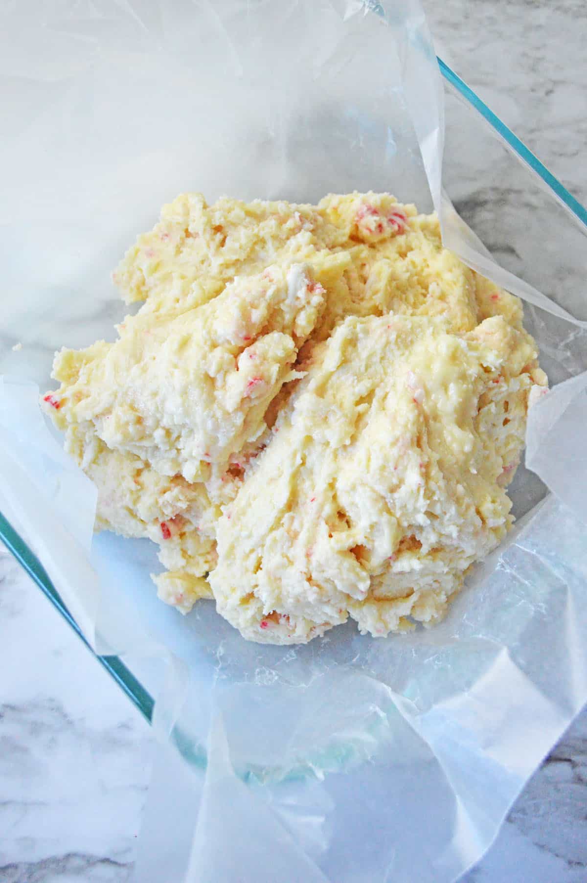 White chocolate chips, condensed milk, and peppermint candies combined in a glass baking pan.