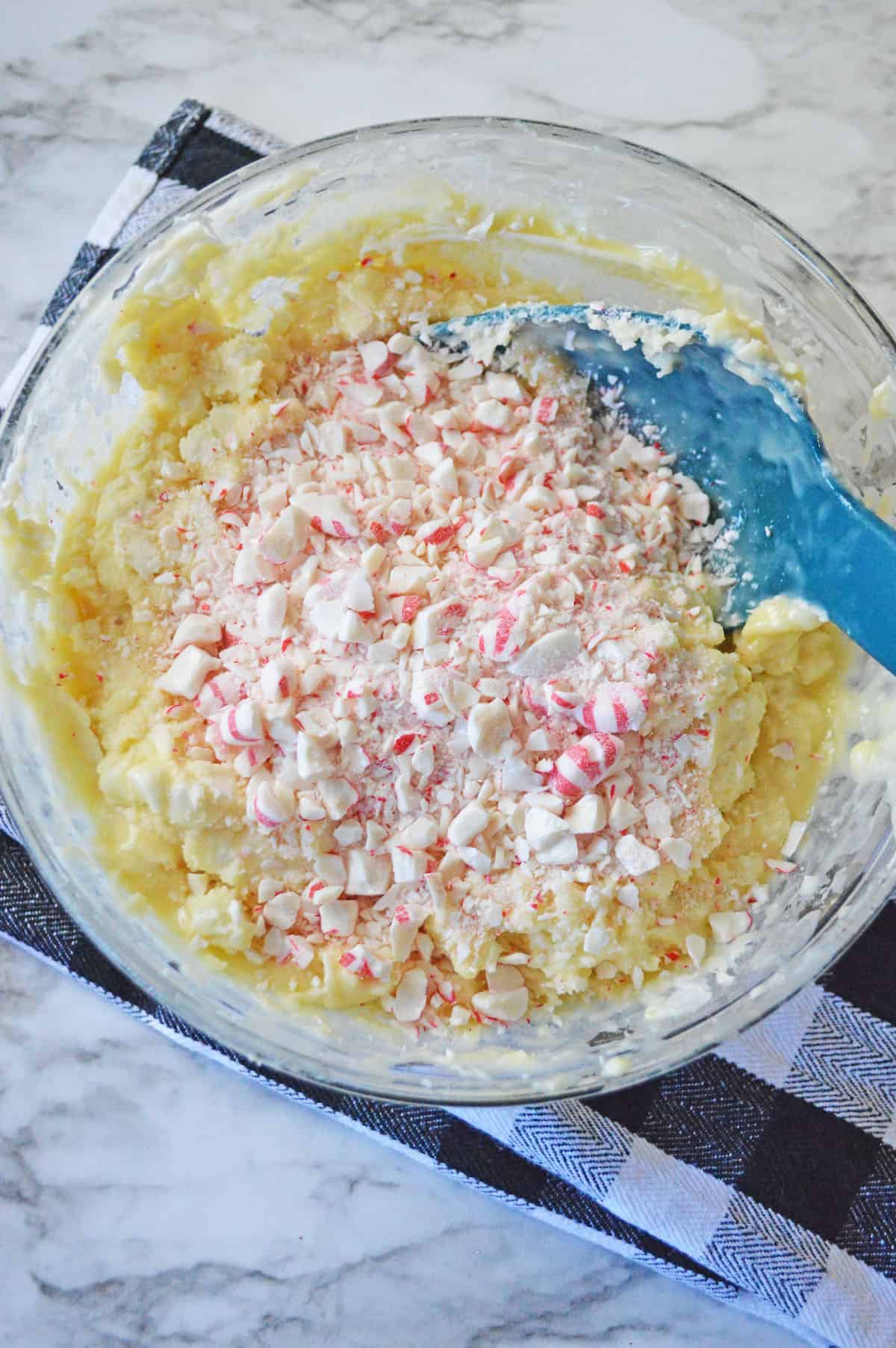 White chocolate chips, condensed milk, and crushed peppermint candies in a glass bowl.