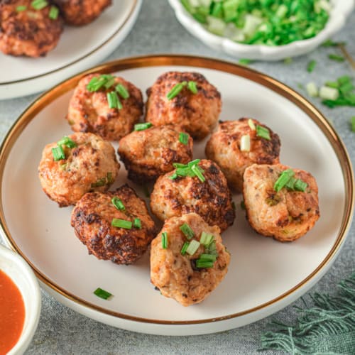 Chicken meatballs sprinkled with green onions on a white plate.