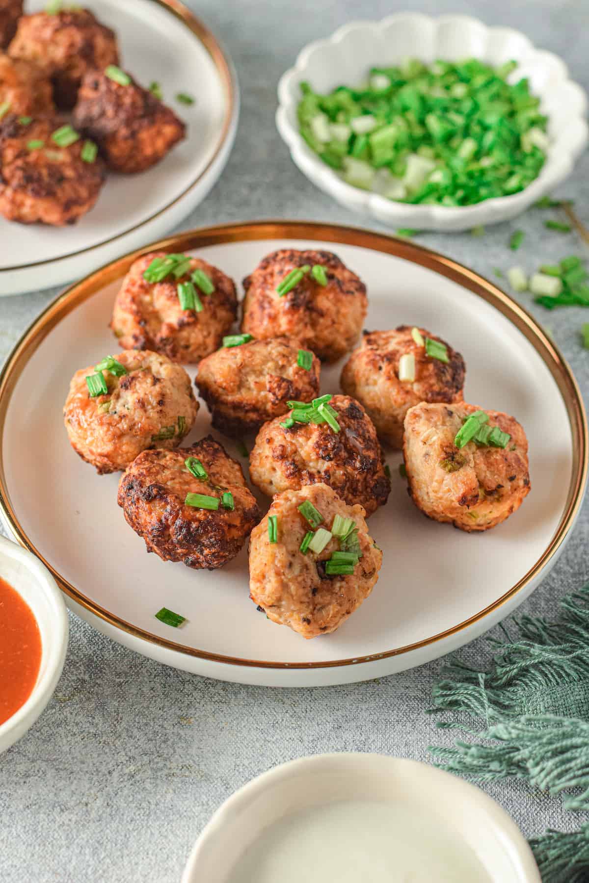 Meatballs on a white plate with green onions and more meatballs in background.