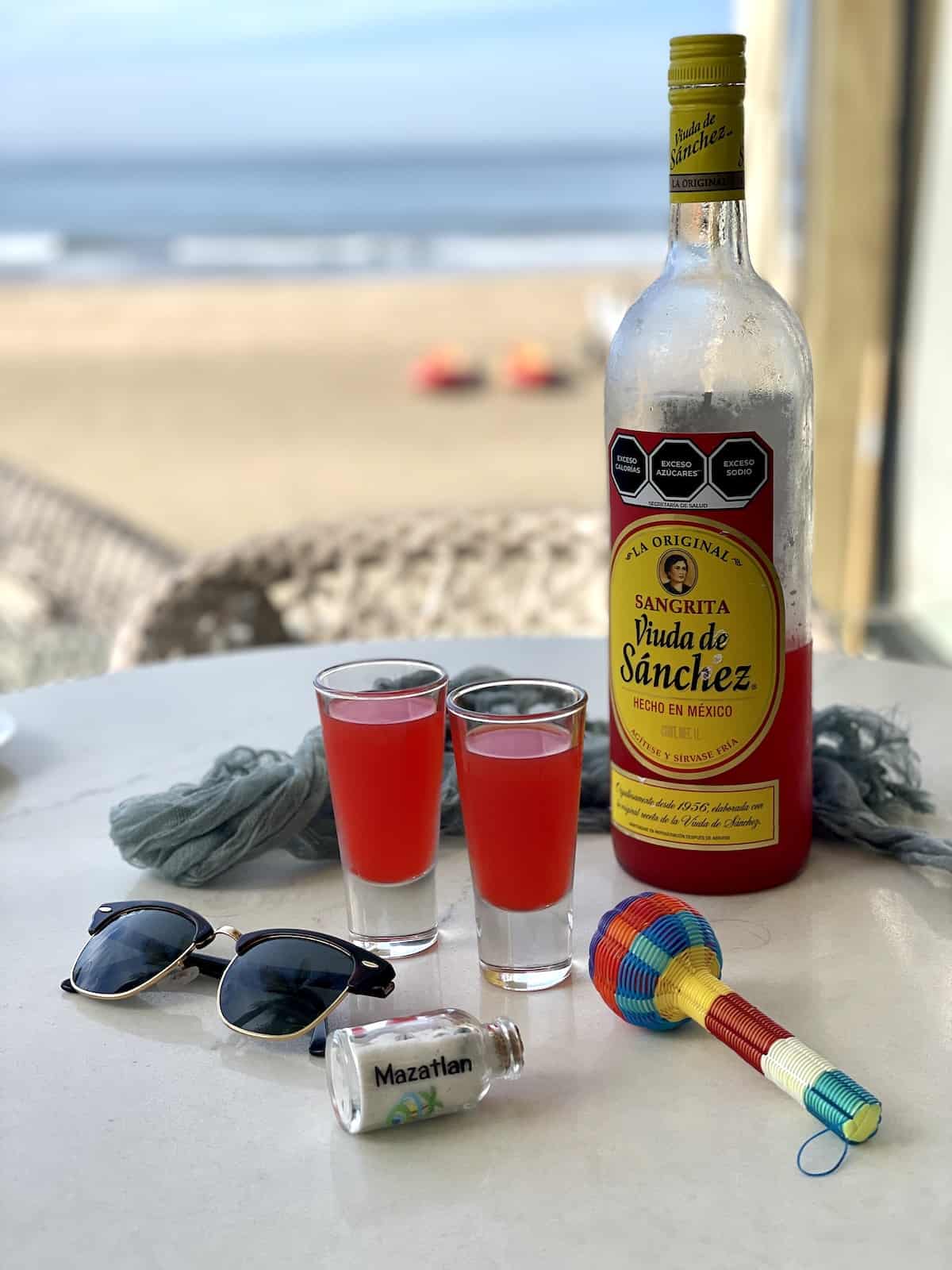 Bottle of Sangrita on white table with sunglasses and souvenirs.