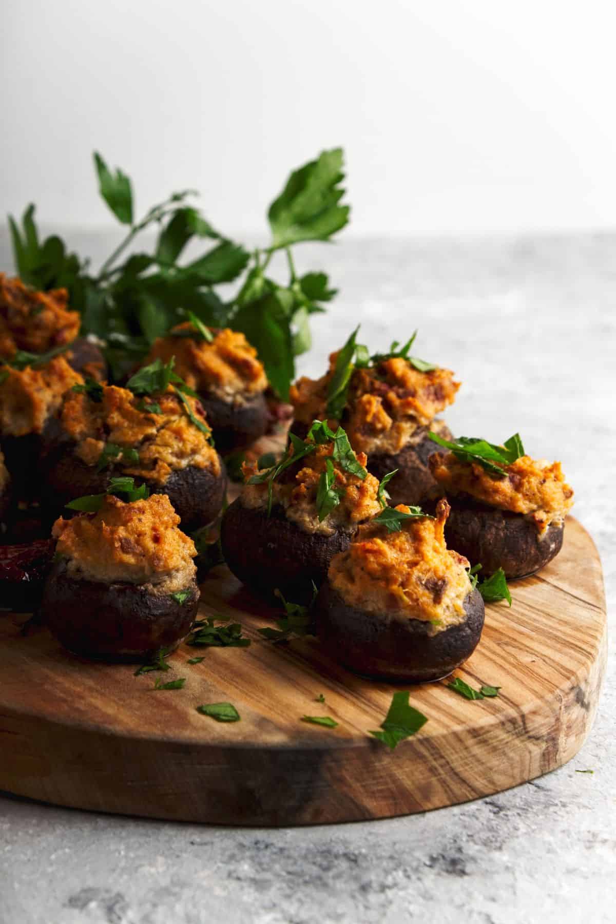 Stuffed mushrooms topped with parsley on a wood board.