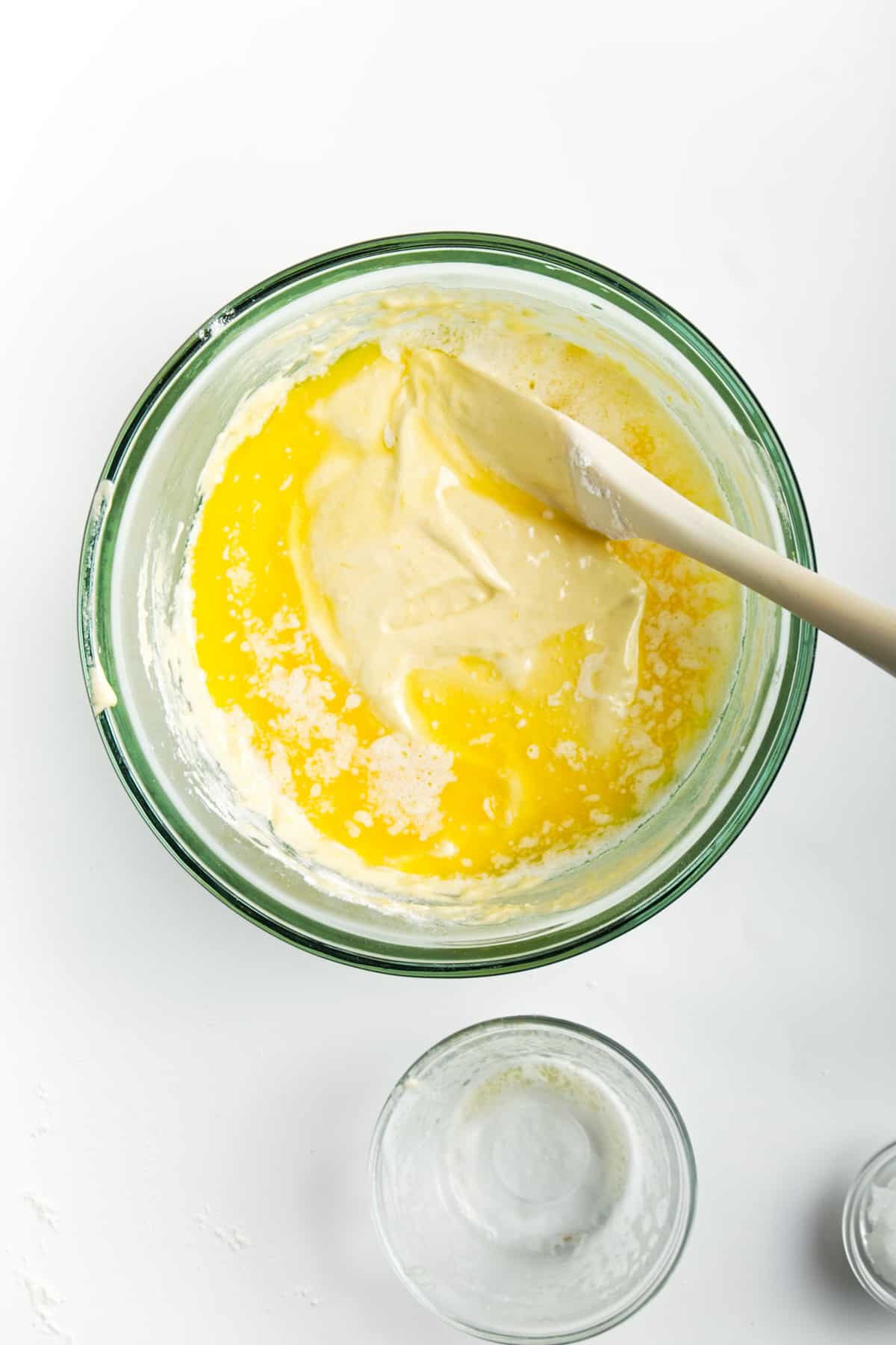 Adding butter to cookie batter in a glass bowl.
