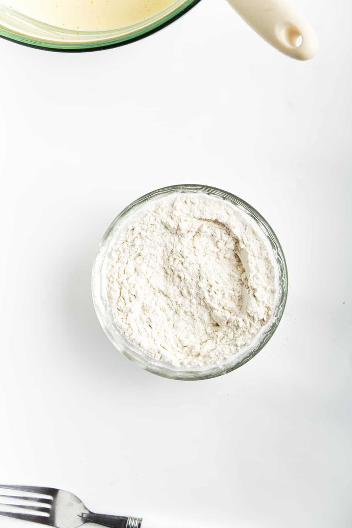 Flour, salt, baking powder in a glass bowl on a white counter.