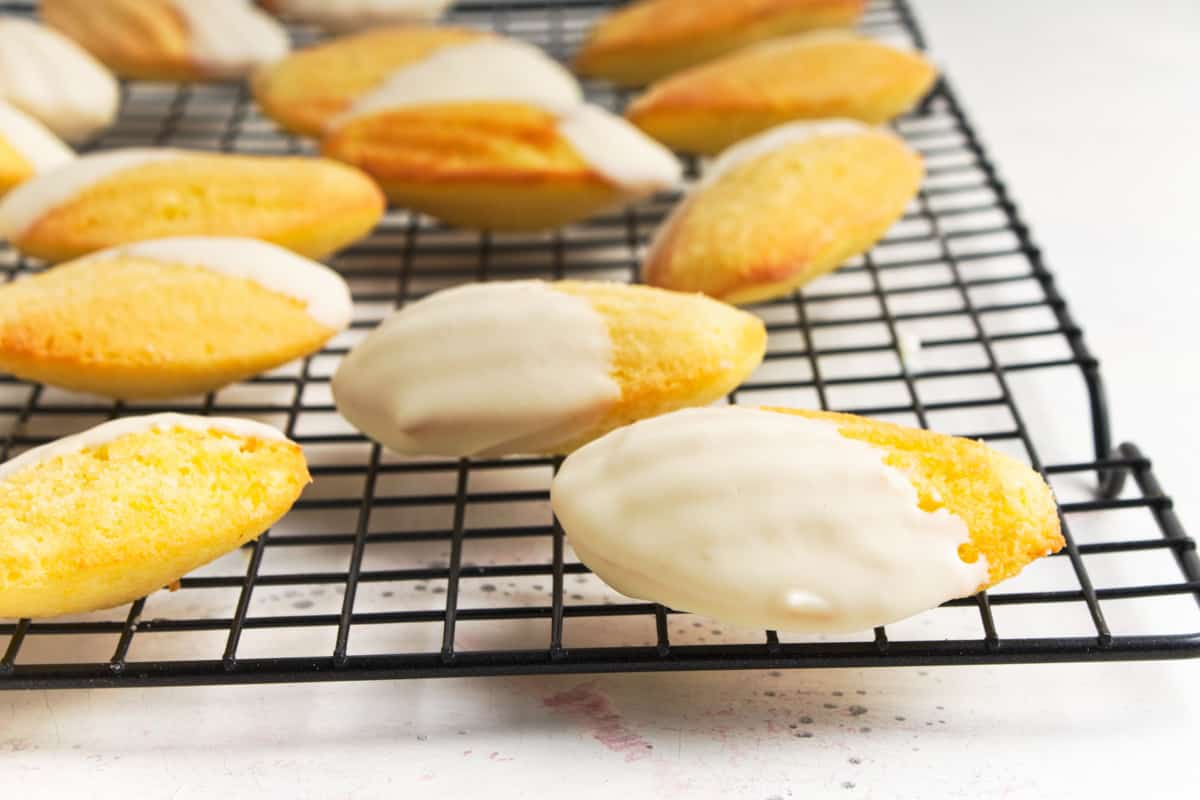 Madeleine cookies dipped in white chocolate on a wire rack.