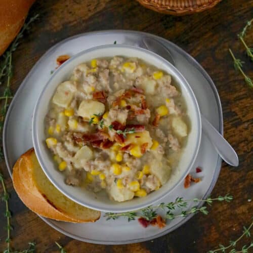 Bowl of corn chowder on a saucer with slice of bread.