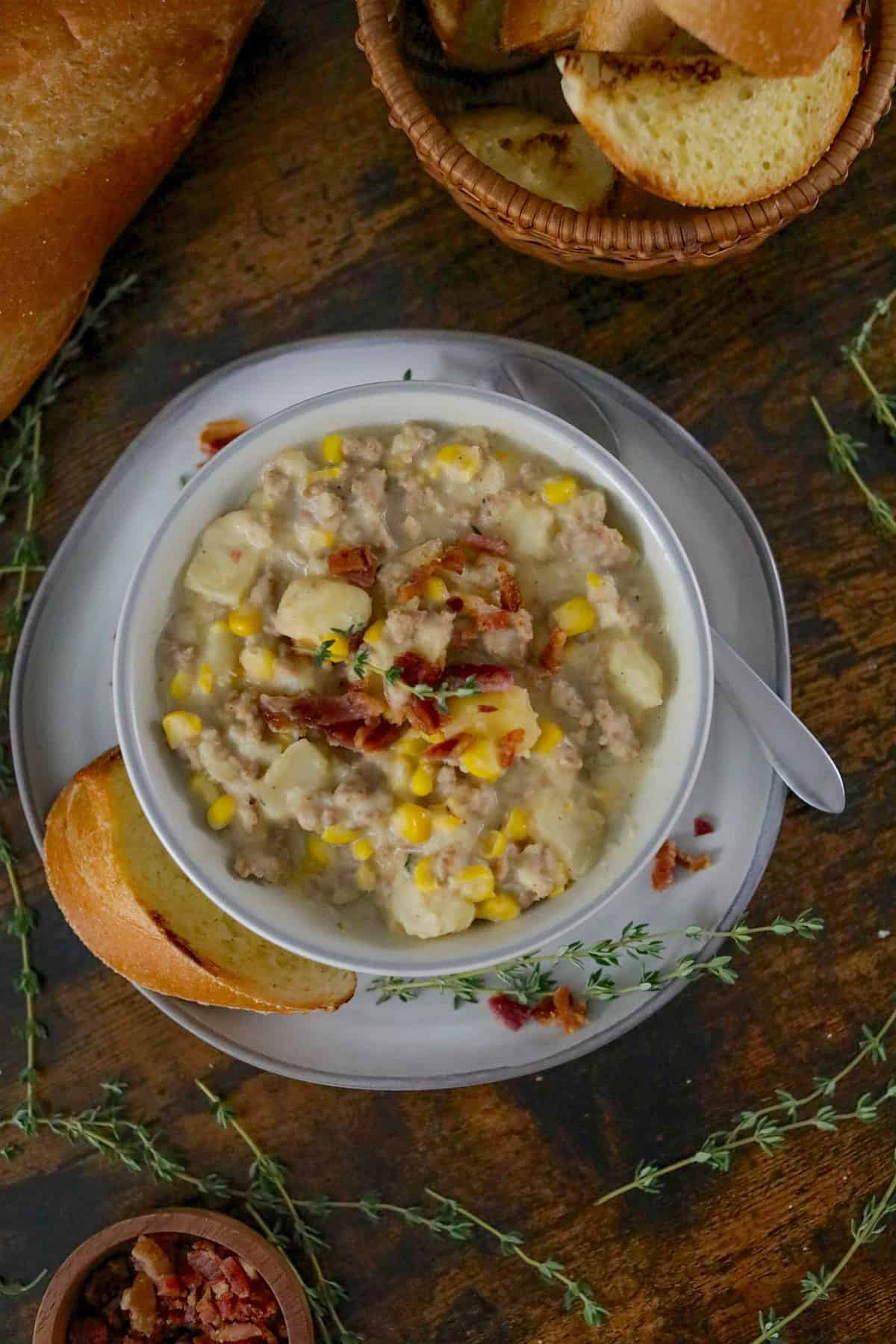 Bowl of corn chowder with sausage in a white bowl on a wood table.