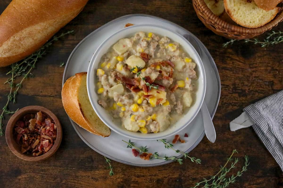 Bowl of corn chowder with sausage in a white bowl on a wood table.