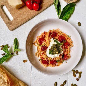 Pasta with tomatoes, ricotta, and pesto in a white bowl on a white table.