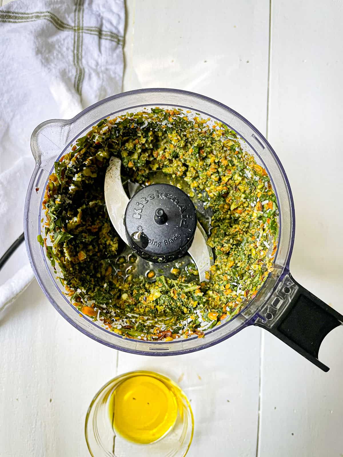 Ingredients to make pistachio pesto blended in a food processor with olive oil on the side.