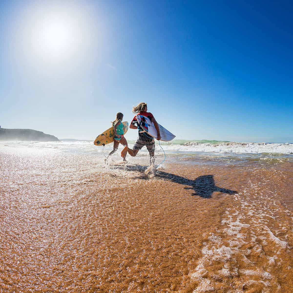 Teens running on beach with surfboards.