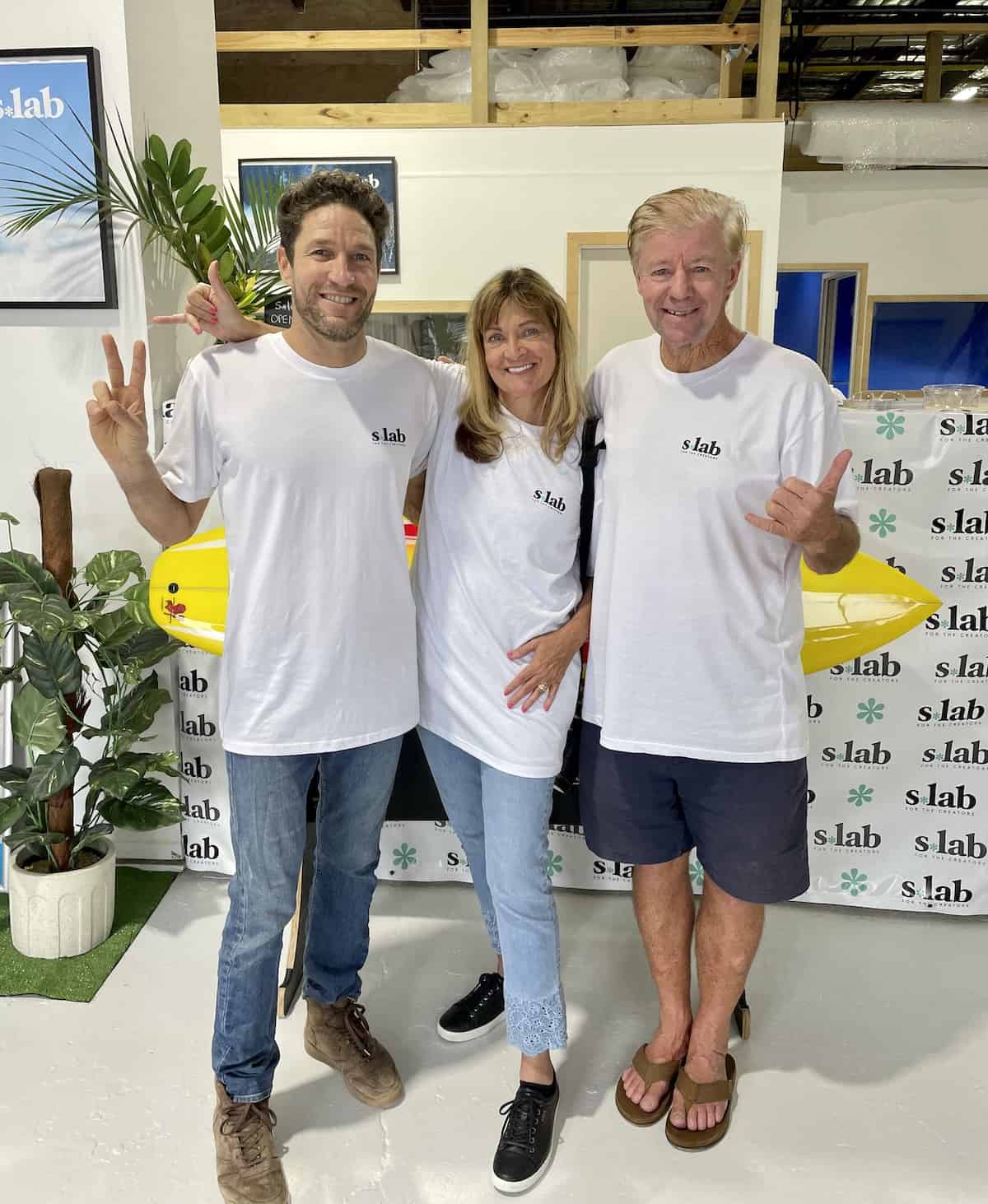 Two men and a woman in white t-shirts at a surf shop.